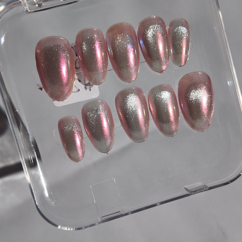 A set of metallic pink press-on nails with a pearlescent shimmer, displayed inside a clear plastic case on a light gray surface.