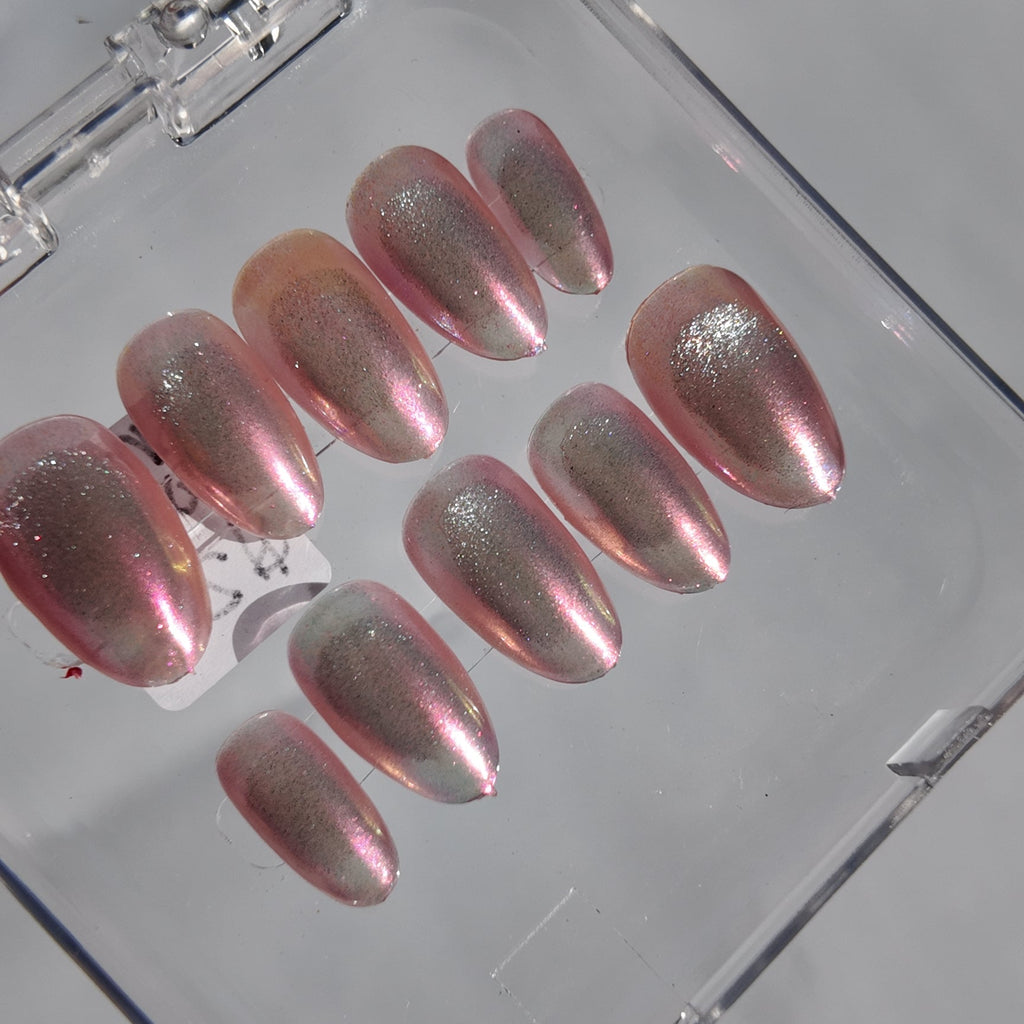 A set of metallic pink press-on nails with a shimmering finish, displayed inside a clear plastic case on a light gray surface.