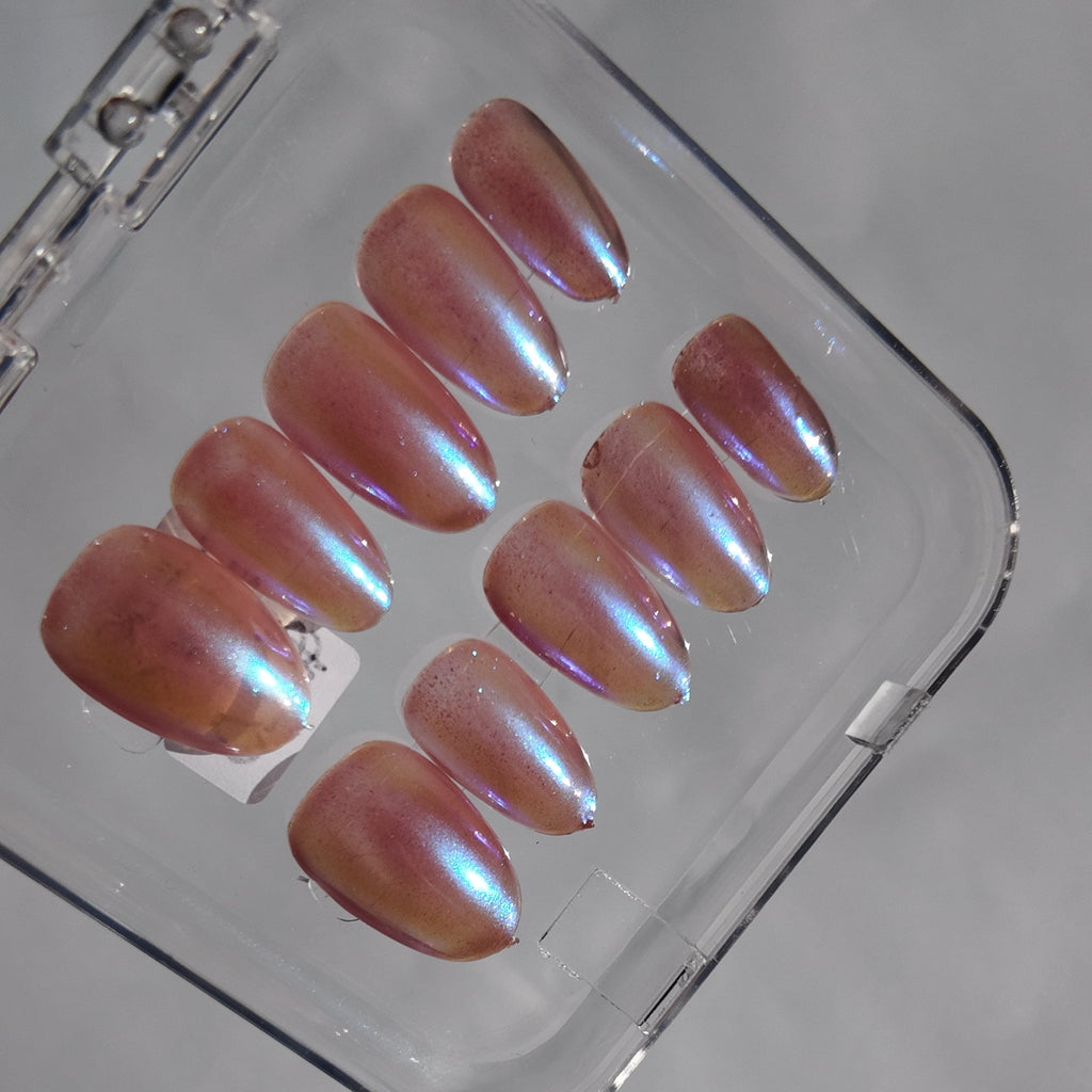 Ten press-on nails with a pearlescent iridescent finish, displayed inside a clear plastic case on a light gray surface.