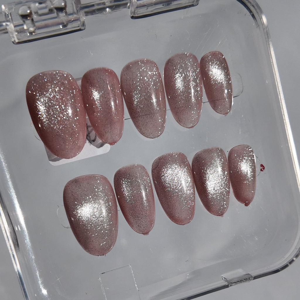 A set of ten false press-on nails with a metallic silver glitter finish and a pinkish nude base, displayed inside a clear plastic case on a light gray surface.